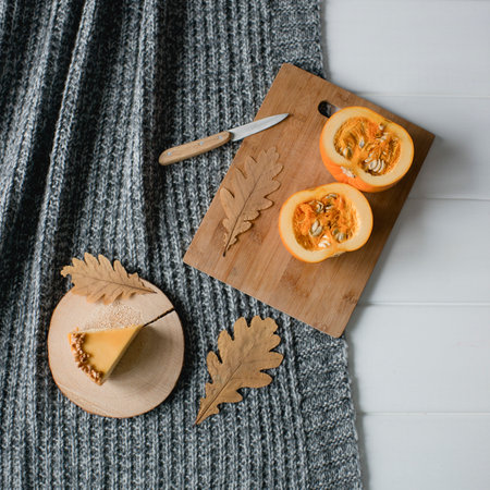 top view of cut half of pumpkin on wooden cutting board, knife and oak leaves on gray knitted sweaterの写真素材