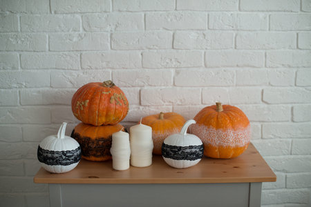 Halloween pumpkins and candles on a wooden table in front of a white brick wallの写真素材