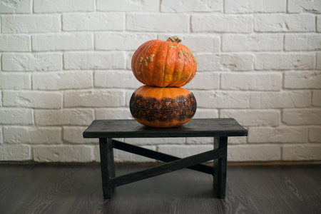 Two pumpkins on a wooden stand against a white brick wall.の写真素材