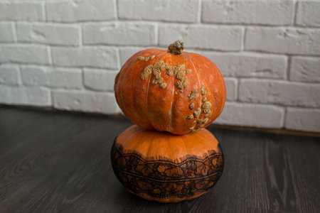 Two pumpkins on a wooden floor against a white brick wall.の写真素材