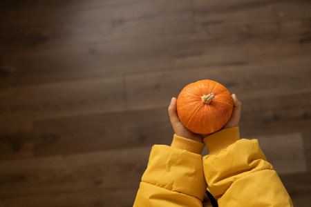 Hands of a child in a yellow raincoat holding a pumpkinの写真素材