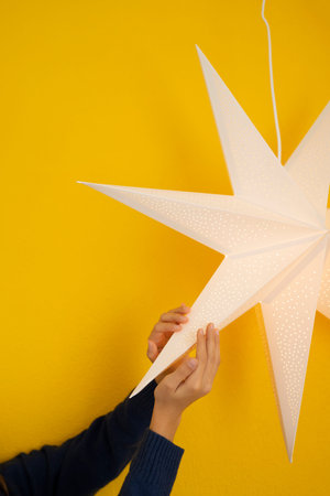 Female hands holding a paper star on a yellow background.
