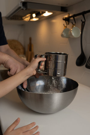 A child and father is cooking in the kitchen at home. They is adding flour to the bowl.