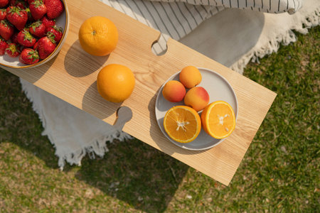 Top view of plate with oranges and strawberries on wooden table in garden