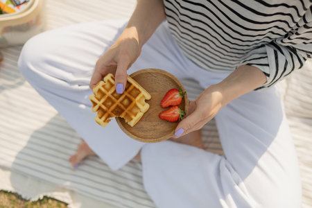 cropped shot of woman holding waffles and strawberries on wooden plateの写真素材