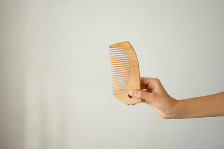 Female hand holding wooden comb against white background, closeup of photoの写真素材