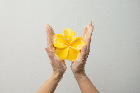 Female hands holding soap in the shape of a yellow flower against a white wall. Handmade soap for the bathroom.の写真素材