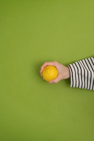 Female hand holding a lemon on a green background. Top view.の写真素材
