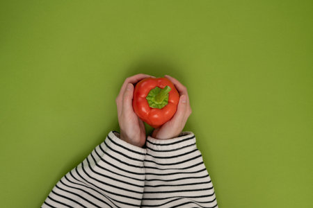 Female hands holding a red bell pepper on a green background. Top viewの写真素材