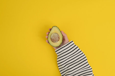 Avocado in woman's hand on yellow background. Flat lay, top view