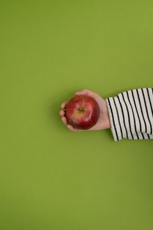 Female hand holding a red apple on a green background, top viewの写真素材