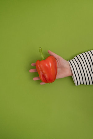 Female hand holding a red pepper on a green background. Top viewの写真素材