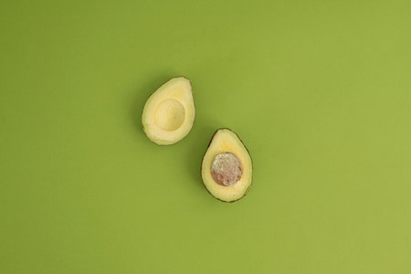 Two halves of avocado on green background. Minimal food concept.の写真素材