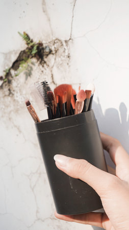 Hands holding clean black vector set of professional makeup concealer powder blush eye shadow eyebrow brush with black handles and makeup palette.の写真素材