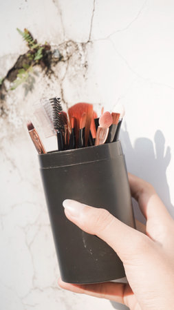 Hands holding clean black vector set of professional makeup concealer powder blush eye shadow eyebrow brush with black handles and makeup palette.の写真素材
