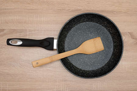 new black round frying pan with a wooden spatula top view for cooking, frying on a wooden table, background, kitchen, isolated, dishes, cookingの写真素材