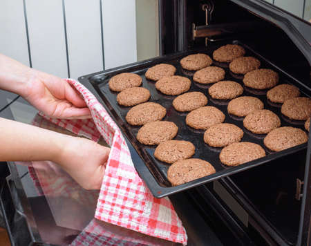 woman takes out a baking sheet with cooked cookies from the ovenの写真素材