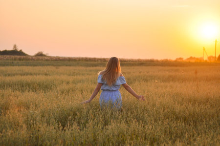 Young girl with long hair walking in the Russian field at sunset