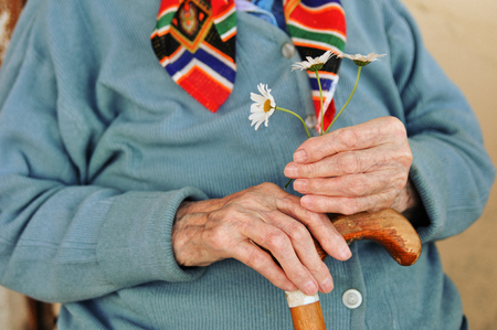 an elderly woman holding flowers and a wooden cane in the street.の写真素材