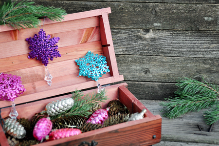 Mahogany wooden box with Christmas tree decorations, gold cones and pine branches on wooden gray background. Winter holidays concept.の写真素材