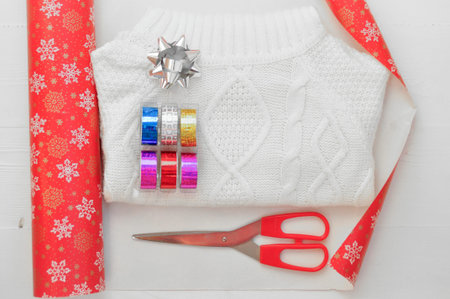 The packaging process of the white knitted sweater. Wrapping paper with snowflakes, colored tape,...