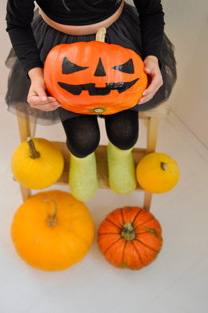The little girl is holding a scary pumpkin for Halloween, sitting on a bench surrounded by other pumpkins. Closupの写真素材