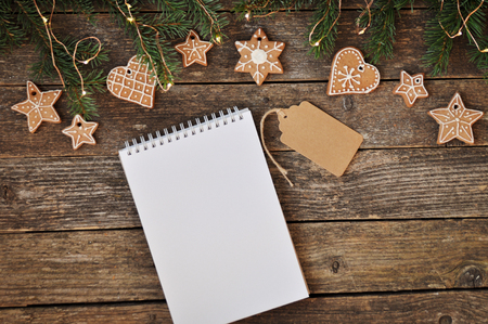 Merry christmas holiday decoration background. Traditional homemade Christmas gingerbread with icing sugar and writing pad on wooden background. Christmas tree decorated with lights. Copy spaceの写真素材