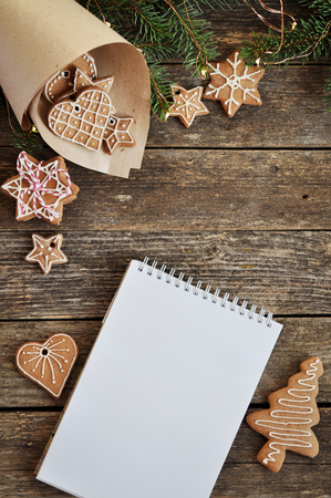 Merry christmas holiday decoration background. Traditional homemade Christmas gingerbread with icing sugar and writing pad on wooden background. Christmas tree decorated with lights. Copy spaceの写真素材