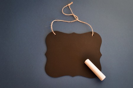 Patterned black wooden chalk Board with a piece of chalk on a dark blue background suitable for greeting, message, menu or purposes. copyspace. top view.の写真素材
