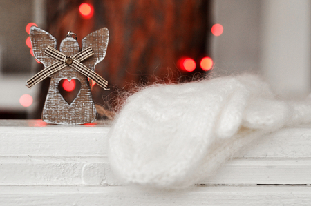 Cute wooden angel decoration on the Christmas tree and white knitted mittens on the background of red lights on the streetの写真素材