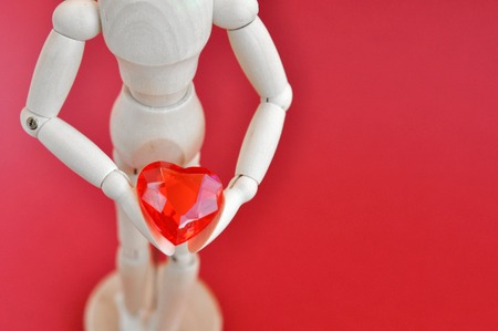 Bright concept for Valentines day. Wooden model of a man holding a red heart on a red background.の写真素材