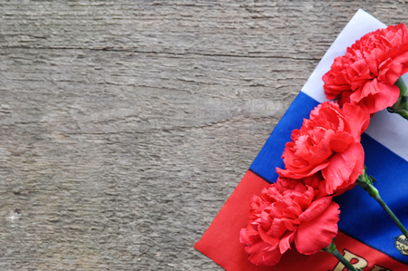 Bright holiday card on February 23. Red carnations and Russian flag on rustic wooden background. Fatherland defender day. The day of military glory.free space for textの写真素材