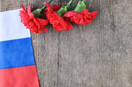 Bright holiday card on February 23. Red carnations and Russian flag on rustic wooden background....