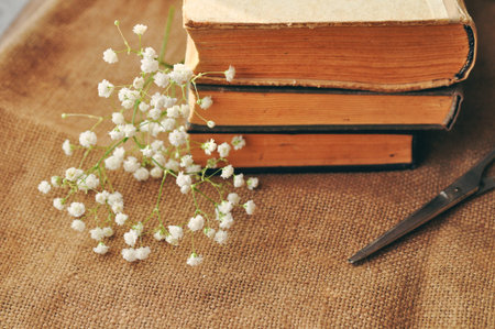 Vintage spring background with white flowers, a yellowed old books and the scissors on the burlap....