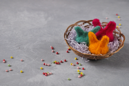 Easter bright handmade Bunny hats for wool eggs in a wicker basket on a gray concrete background. Funny decoration holiday concept. copyspace. top viewの写真素材