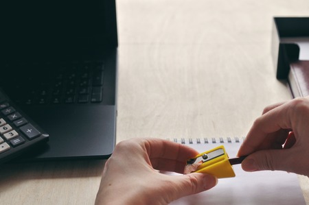 A womans hand is sharpen pencil sharpener over the Desk close-up. Study and education conceptの写真素材