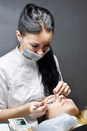 Eyelash Extension Procedure. Woman hands Closeup with tool for eyelash extension. Master of tweezers is working.の写真素材