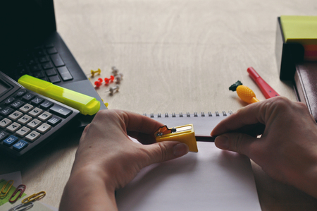 A womans hand is sharpen pencil sharpener over the Desk close-up. Study and education conceptの写真素材