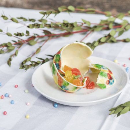 Easter eggs of white chocolate handmade on the table decorated with satin ribbons, green branches,...