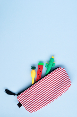 Bright stationery pens in the form of a cactus, watermelon, pineapple in a pencil case on a blue background. Back to school. Top view. Copy spaceの写真素材
