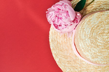 Beautiful pink peony flower next to straw hat on red background.の写真素材