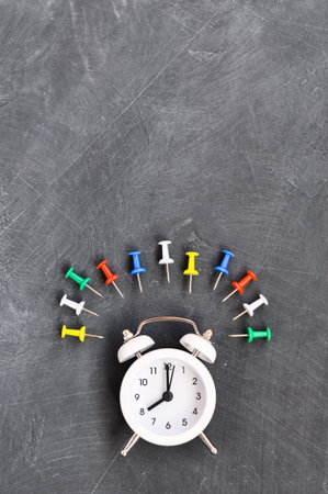 Alarm clock, colored pencils and stationery on black school Board background