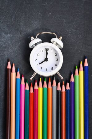 Concept Back To School Alarm clock, colored pencils and stationery on black school Board background. Copy Space. Supplies. Top View Flat Layの写真素材