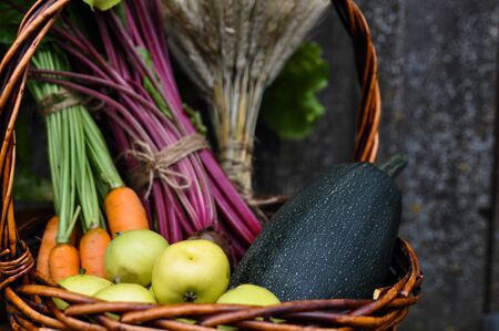 Basket with gifts of autumn consisting of carrots, beets, zucchini, apples, wheat on an old chair . Harvest. Selective focus.の写真素材