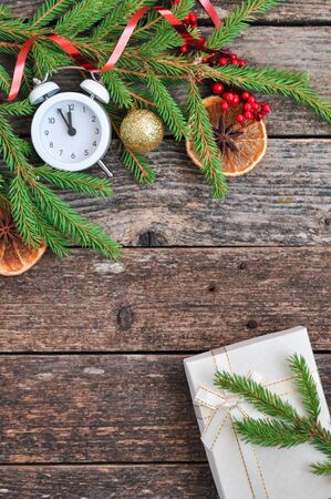 Holiday Christmas card with fir branches, Holly berries, dried oranges, gift, and alarm clock on rustic wooden background. top viewの写真素材