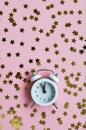 White alarm clock and star confetti on pink delicate background for holiday time. Flatley.の写真素材