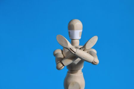 A figure of a man made of wood in a medical mask holds his hands up, warning of danger. Coronavirus, pandemic and epidemic conceptの写真素材