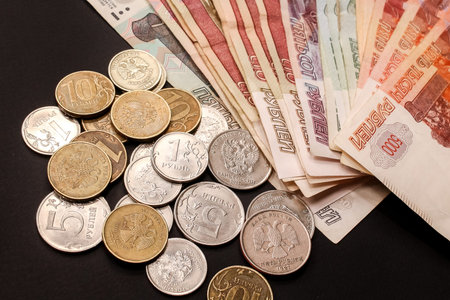Russian cash money. Close-up of rubles coins of different value and a stack of banknotes on black...