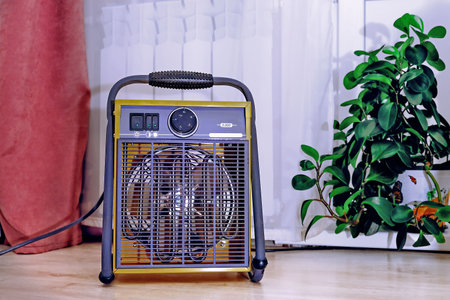 Modern electric fan heater on the floor in the kitchen next to a cold radiatorの写真素材
