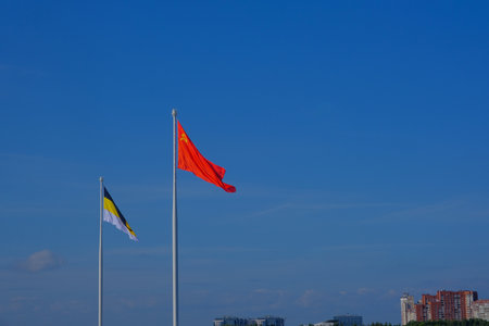 Two large flagpoles with the flags of the Soviet Union and the Russian Empire on a blue sky background.の写真素材